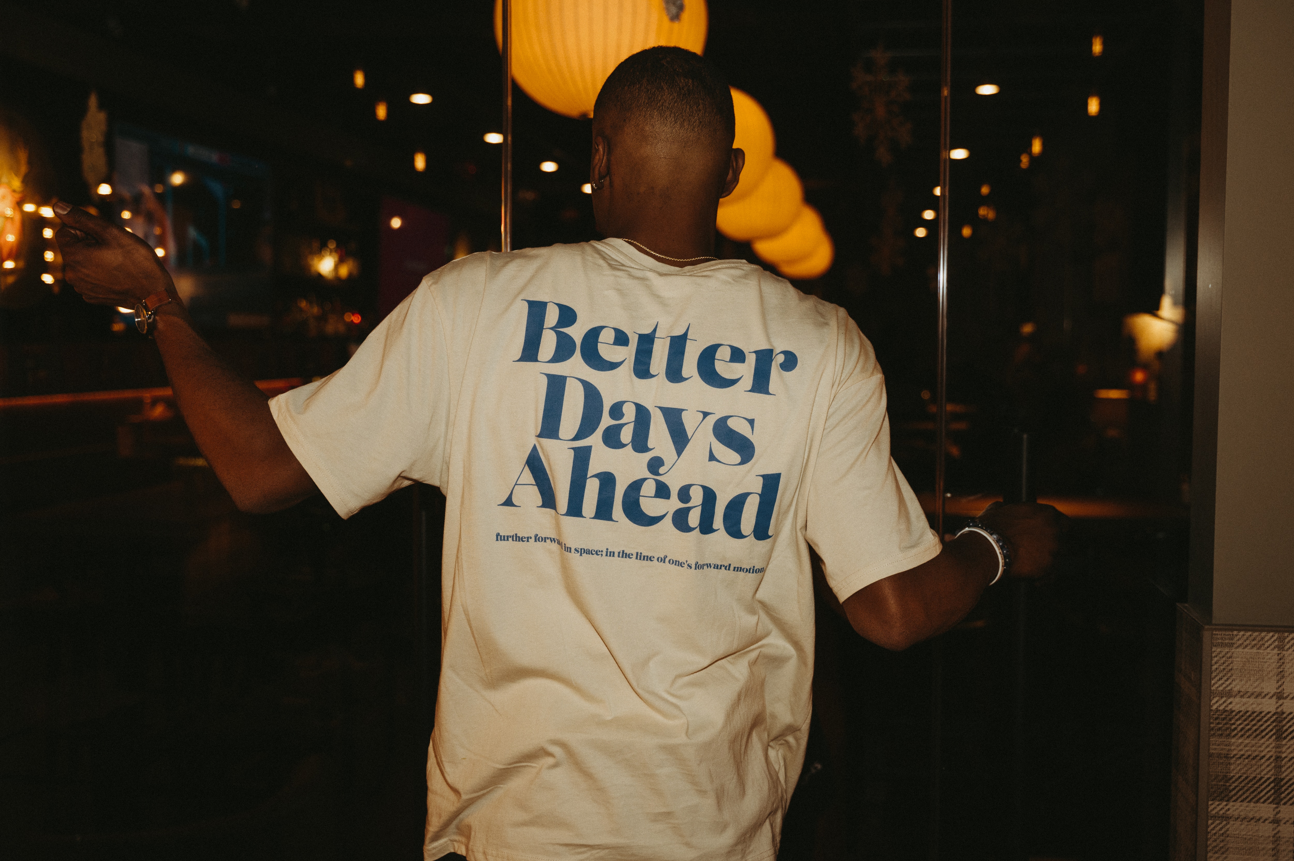 A person turning towards the camera, wearing a white T-shirt with "Better Days Ahead" printed on the back in blue letters.