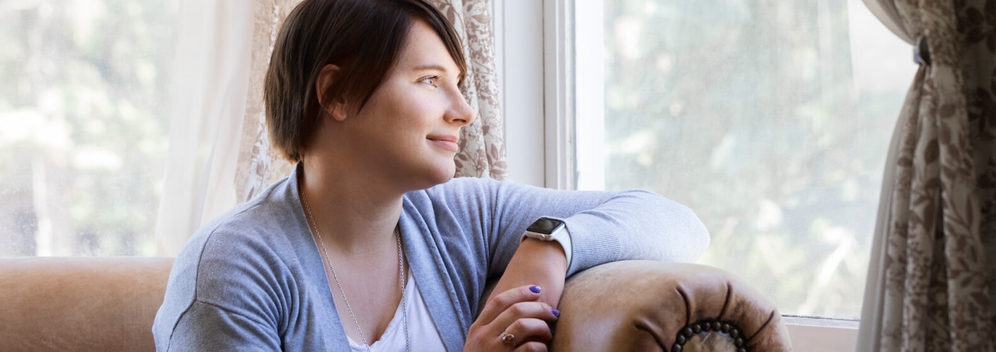 Image of Sarah at a window. Sarah uses transanal irrigation to help her manage her bowel issues.